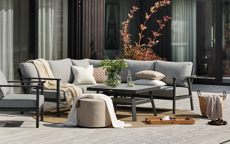 moderne Gartenlounge in grau mit stylischen Outdoor Teppich und Kissen dekoriert.